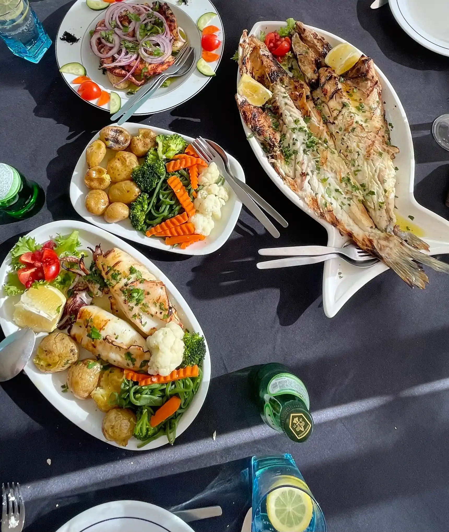 A colorful and fresh Portuguese seafood meal served on a black tablecloth, featuring grilled fish, squid, boiled potatoes, mixed vegetables, and a salad. Captured during a Yes, You Deserve tour lunch stop in Sintra.