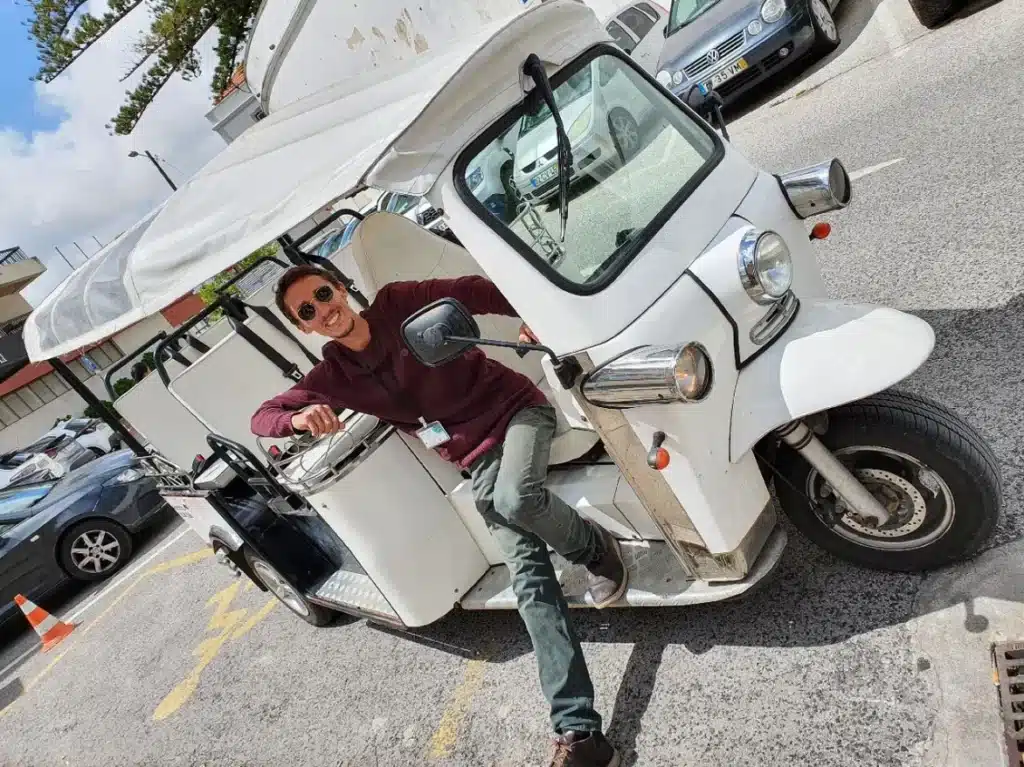 Daniel Ponce, smiling and wearing sunglasses, poses confidently in the driver’s seat of a white electric tuk-tuk during a Yes, You Deserve tour in Sintra, ready to lead another unforgettable adventure.