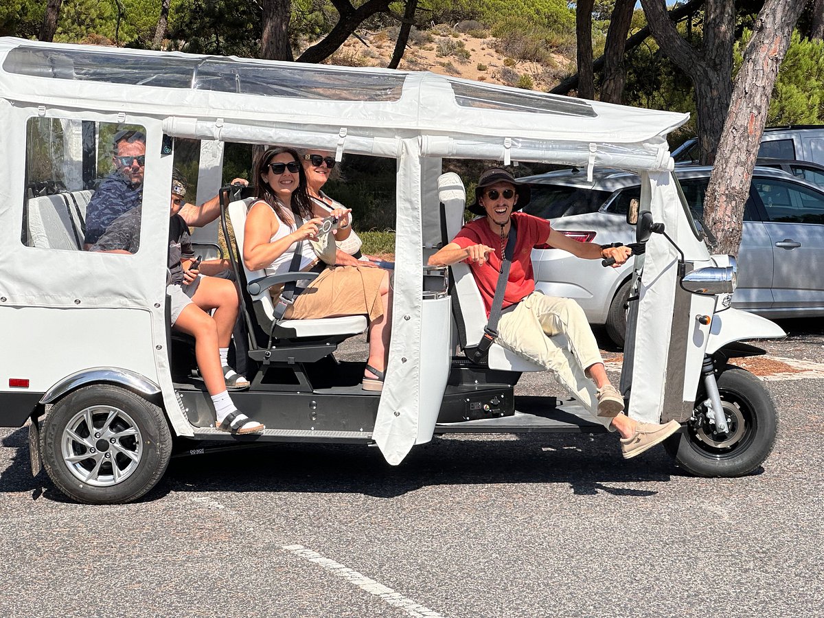 Daniel Ponce drives a white electric tuk-tuk filled with smiling tourists during a sunny Yes, You Deserve tour in Sintra. The group looks excited and ready to explore, enjoying a fun and eco-friendly ride through scenic landscapes.