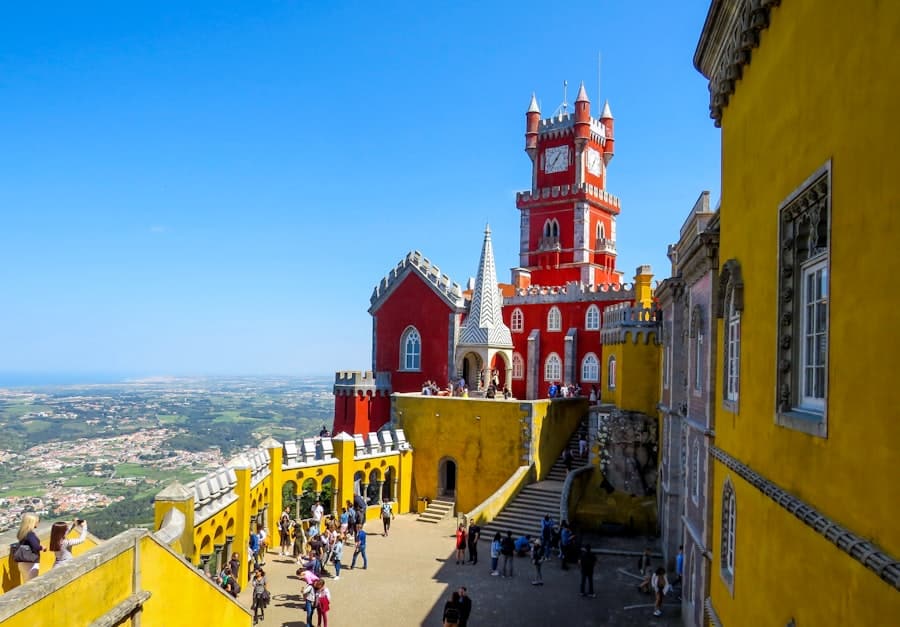 Colorful courtyard and panoramic view from Pena Palace in Sintra, Portugal, with tourists exploring the red, yellow and tiled sections of the romantic palace — part of a guided Yes, You Deserve tuk tuk experience.