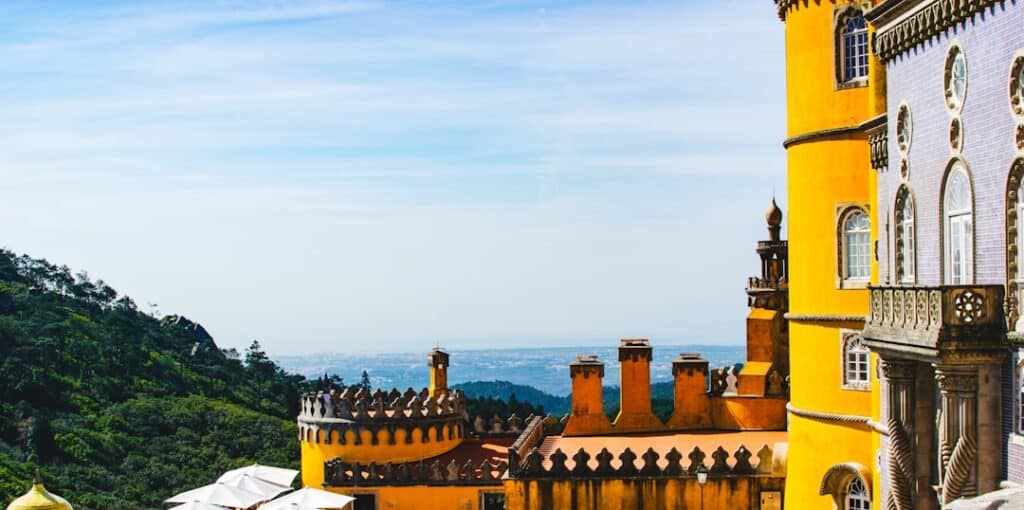 View from Pena Palace in Sintra, Portugal, highlighting the vibrant yellow walls, intricate tilework, and panoramic landscape stretching to the Atlantic Ocean — part of Yes, You Deserve’s private tuk tuk tour experience.
