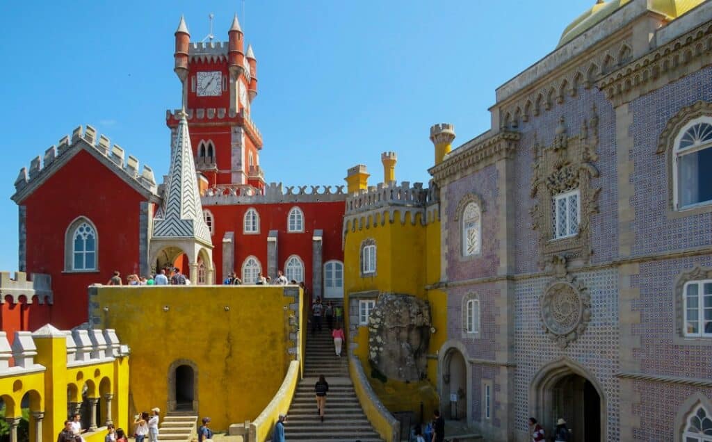 Colorful courtyard of Pena Palace in Sintra, Portugal, featuring its iconic red, yellow, and tiled façades with visitors exploring — a must-see destination on the Yes, You Deserve private tuk tuk tours.