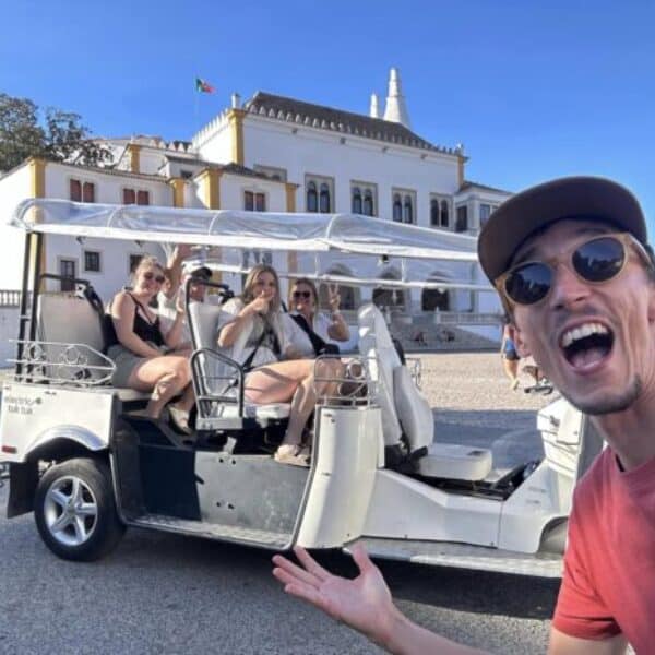 Happy tuk tuk guide and group of tourists in front of the National Palace of Sintra during a private tour in Portugal.