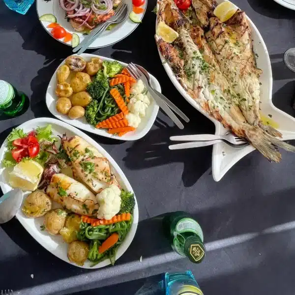 A colorful and fresh Portuguese seafood meal served on a black tablecloth, featuring grilled fish, squid, boiled potatoes, mixed vegetables, and a salad. Captured during a Yes, You Deserve tour lunch stop in Sintra.