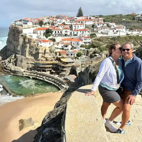 Couple enjoying the view at Azenhas do Mar, a stunning cliffside village near Sintra, Portugal, during a tour with the company Yes, You Deserve. The ocean, natural pool, and traditional white houses with red roofs create a picturesque backdrop.