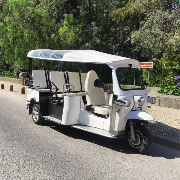 A white electric tuk-tuk parked on a quiet road in Sintra, Portugal, ready to take guests on a scenic and eco-friendly adventure with Yes, You Deserve. Surrounded by lush greenery and cobblestone paths, it offers a charming and sustainable way to explore the town.