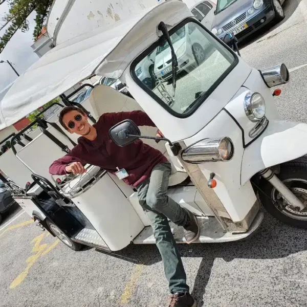Daniel Ponce, smiling and wearing sunglasses, poses confidently in the driver’s seat of a white electric tuk-tuk during a Yes, You Deserve tour in Sintra, ready to lead another unforgettable adventure.