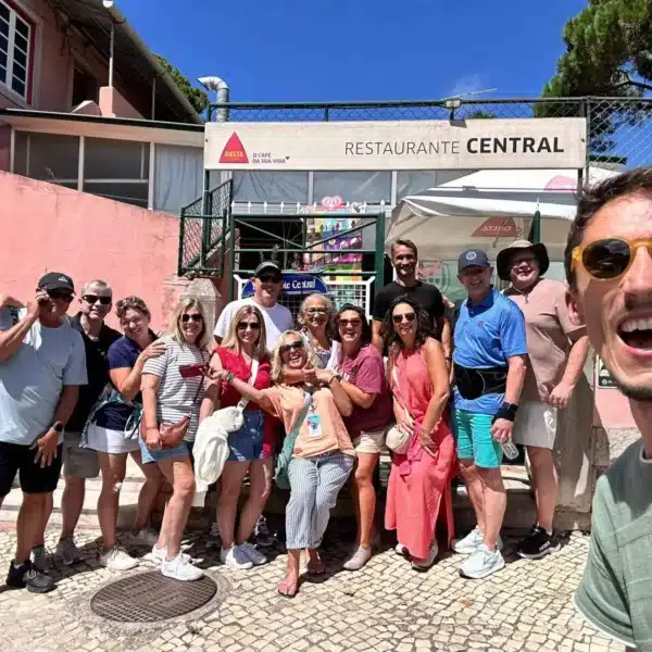 A cheerful group of tourists and their smiling guide pose in front of Restaurante Central in Sintra, Portugal, during a tour with Yes, You Deserve. The sunny day and relaxed atmosphere highlight the joy of the experience.